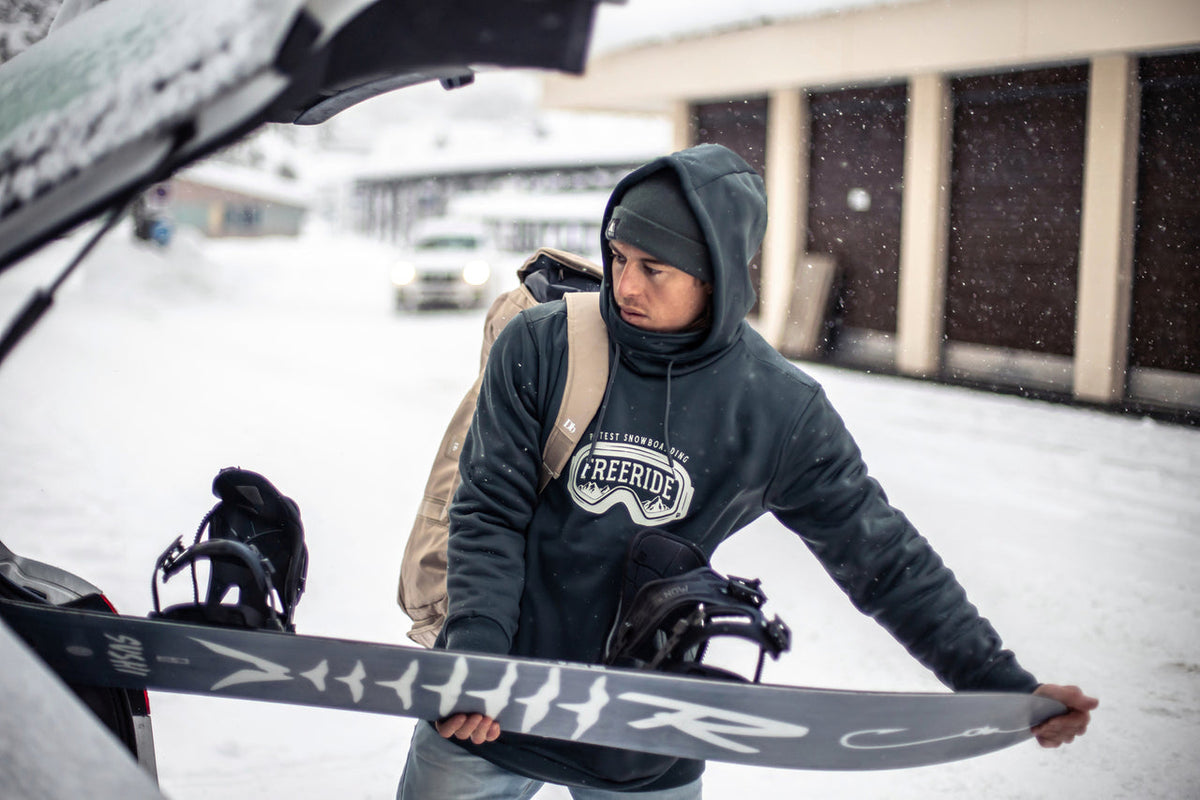 a snowboarder putting a board in the boot of a car
