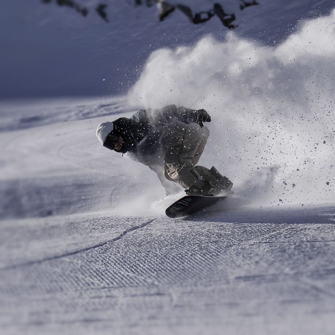 A snowboarder riding in a crouched position kicking snow up behind