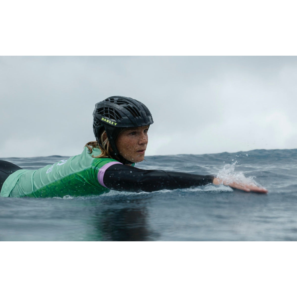 a surfer paddling in the sea wearing an Oakley WTR Icon surf helmet