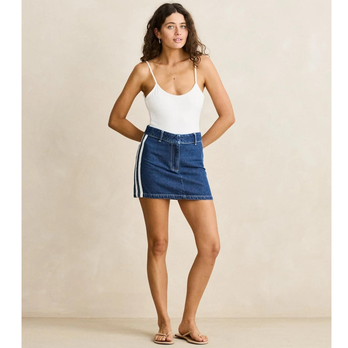 Woman wearing a white tank top and blue denim skirt against a beige background
