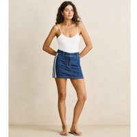 Woman wearing a white tank top and blue denim skirt against a beige background