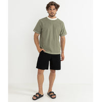 Man wearing a green t-shirt and black shorts standing against a white background