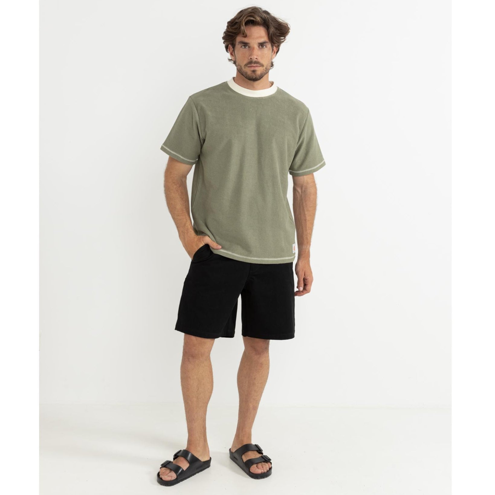 Man wearing a green t-shirt and black shorts standing against a white background