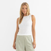 Woman wearing a white sleeveless top and green striped pants on a white background