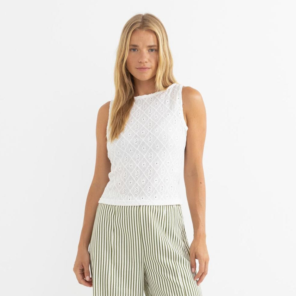 Woman wearing a white sleeveless top and green striped pants on a white background