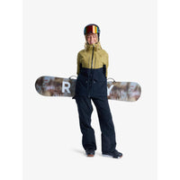 Person wearing a green jacket and black pants holding a snowboard with a visible brand logo on a white background