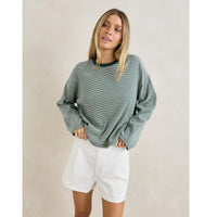 Woman wearing a green sweater and white shorts against a plain background