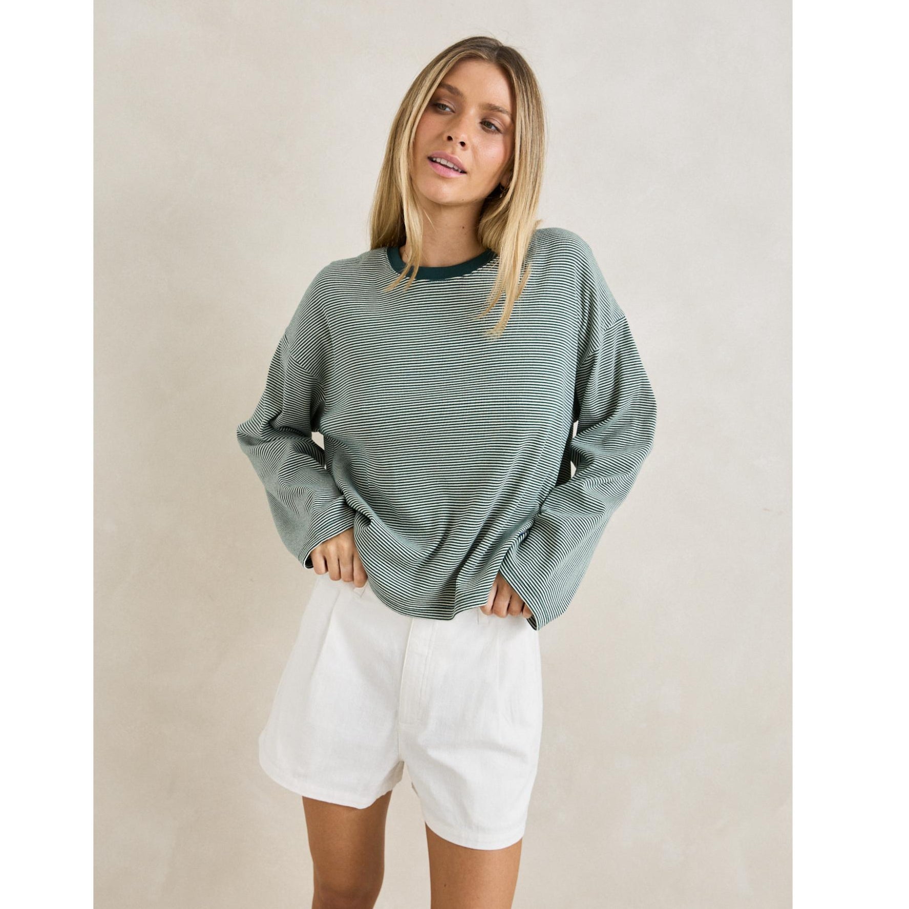Woman wearing a green sweater and white shorts against a plain background